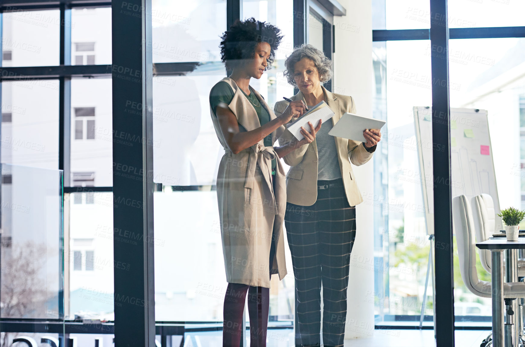 Buy stock photo Shot of two businesswomen making notes while discussing something on a tablet