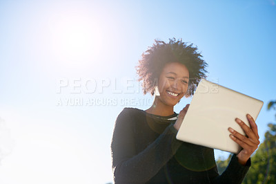 Buy stock photo Low angle shot of an attractive young woman using her tablet outside