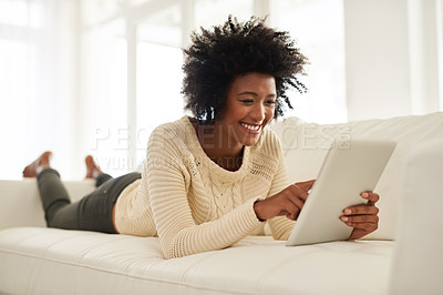 Buy stock photo Shot of an attractive young using her tablet while lying on the sofa at home