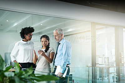Buy stock photo Shot of a business team using a digital tablet while having an informal meeting
