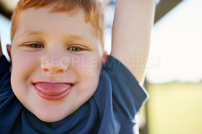 Buy stock photo Portrait of a boy sticking out his tongue while hanging from a jungle gym