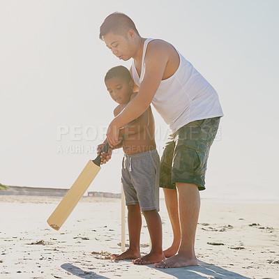 Buy stock photo Shot of a father showing his son how to hold a cricket bat on the beach