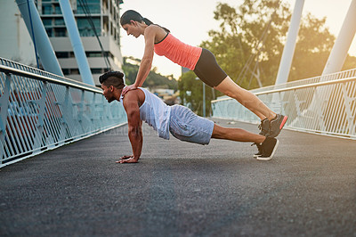 Buy stock photo Shot of a young woman balancing on her boyfriend's back while doing pushups outdoors on a bridge