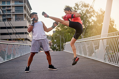 Buy stock photo Shot of a young couple going through some kickboxing routines outdoors on a bridge