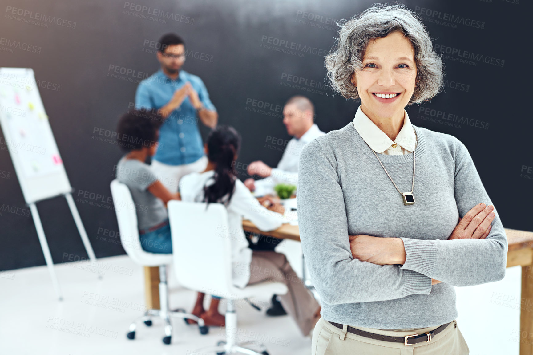 Buy stock photo Portrait of a businesswoman standing with her arms folded in the boardroom while a colleague gives a presentation in the background