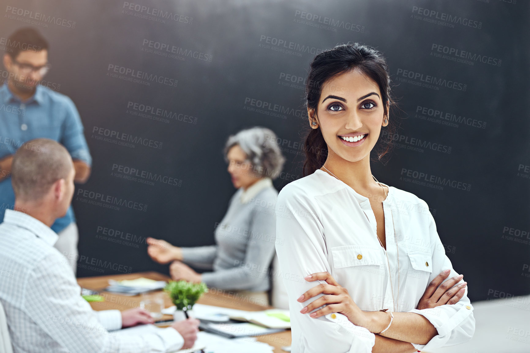 Buy stock photo Portrait of a businesswoman standing with her arms folded in the boardroom while a colleague gives a presentation in the background