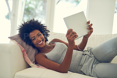 Buy stock photo Portrait of a young woman using her digital tablet while relaxing at home