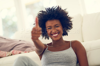 Buy stock photo Portrait of a young woman showing thumbs up while relaxing at home