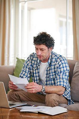 Buy stock photo Shot of a mature man going over his expenses while sitting on the sofa at home
