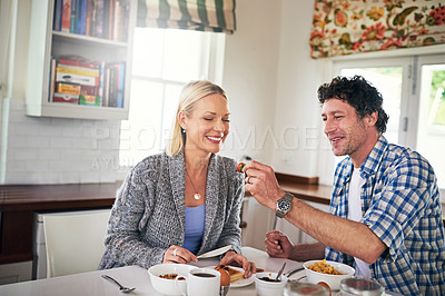 Buy stock photo Shot of a happy couple eating breakfast together in their kitchen at home