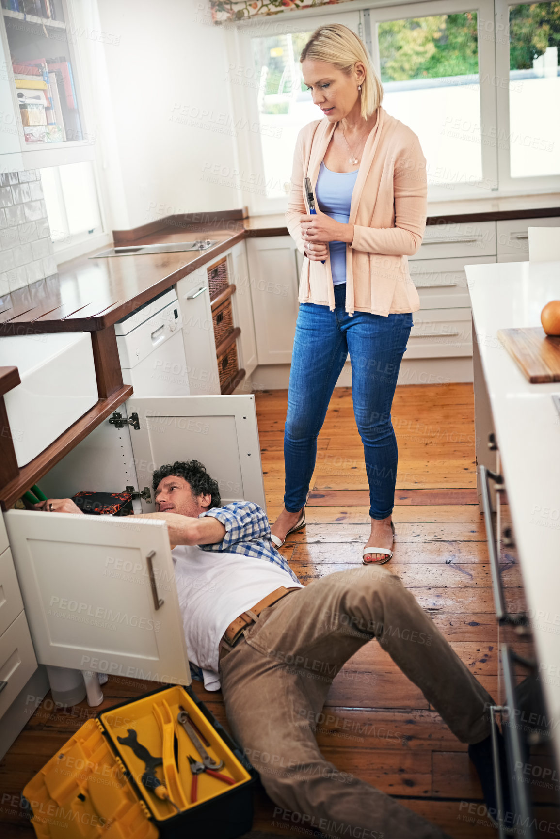 Buy stock photo Plumber, working and woman watching stressed for pipe repairs, sink leaks and kitchen maintenance. Lady, worried and handyman with tools for fixing home basin, drain or broken interior sewer