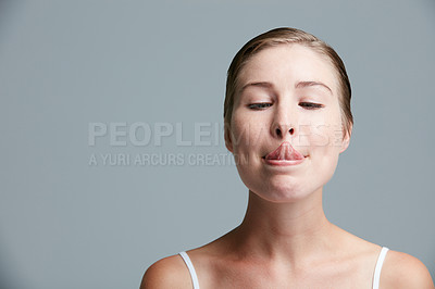 Buy stock photo Studio shot of an attractive young woman trying to touch her nose with her tongue against a gray background