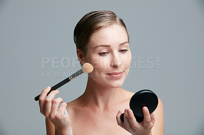 Buy stock photo Studio shot of an attractive young woman applying makeup with a brush against a gray background