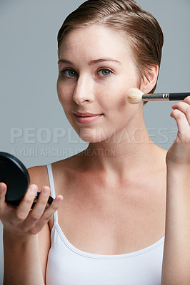 Buy stock photo Studio portrait of an attractive young woman applying makeup with a brush against a gray background