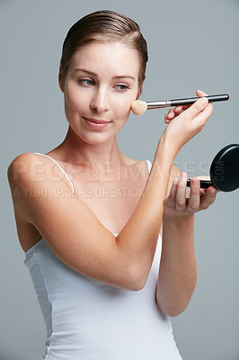 Buy stock photo Studio shot of an attractive young woman applying makeup with a brush against a gray background