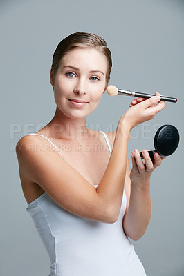 Buy stock photo Studio portrait of an attractive young woman applying makeup with a brush against a gray background