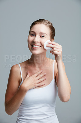 Buy stock photo Studio portrait of an attractive young woman using a cotton pad on her face against a gray background