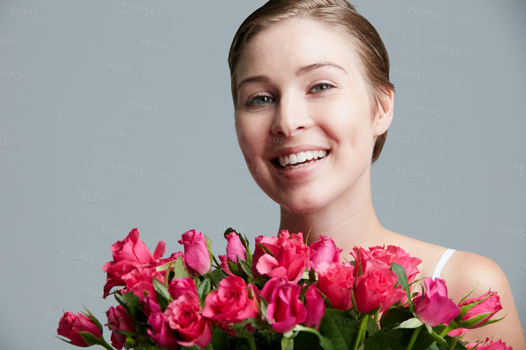 Buy stock photo Studio portrait of an attractive young woman holding a bunch of pink roses against a gray background
