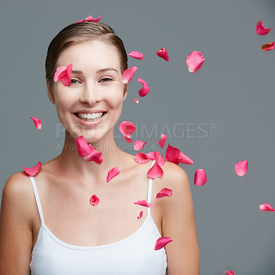 Buy stock photo Studio portrait of an attractive young woman surrounded by falling pink petals against a gray background