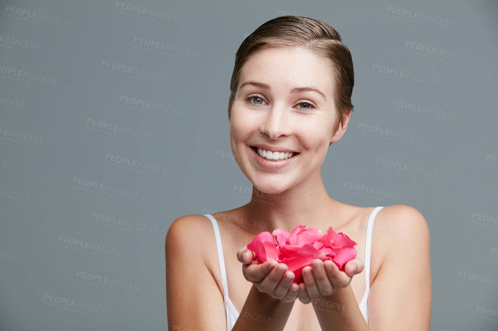 Buy stock photo Studio portrait of an attractive young woman holding a handful of pink petals against a gray background