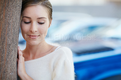 Buy stock photo Shot of a smiling young woman leaning against a tree outside
