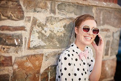 Buy stock photo Portrait of a trendy young woman using her phone while leaning against a wall outside