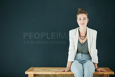 Buy stock photo Portrait of a young businesswoman sitting on a table against a black background