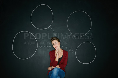Buy stock photo Studio shot of a young woman posing with a chalk illustration of thought bubbles against a dark background