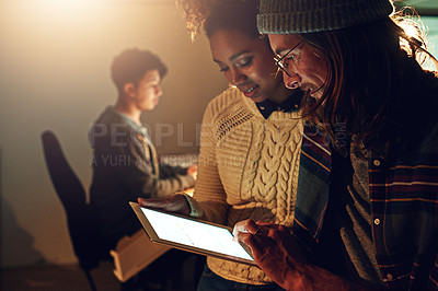 Buy stock photo Shot of two coworker discussing something on a digital tablet while working night shift at the office