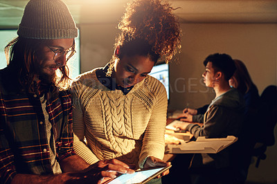 Buy stock photo Shot of two coworker discussing something on a digital tablet while working night shift at the office