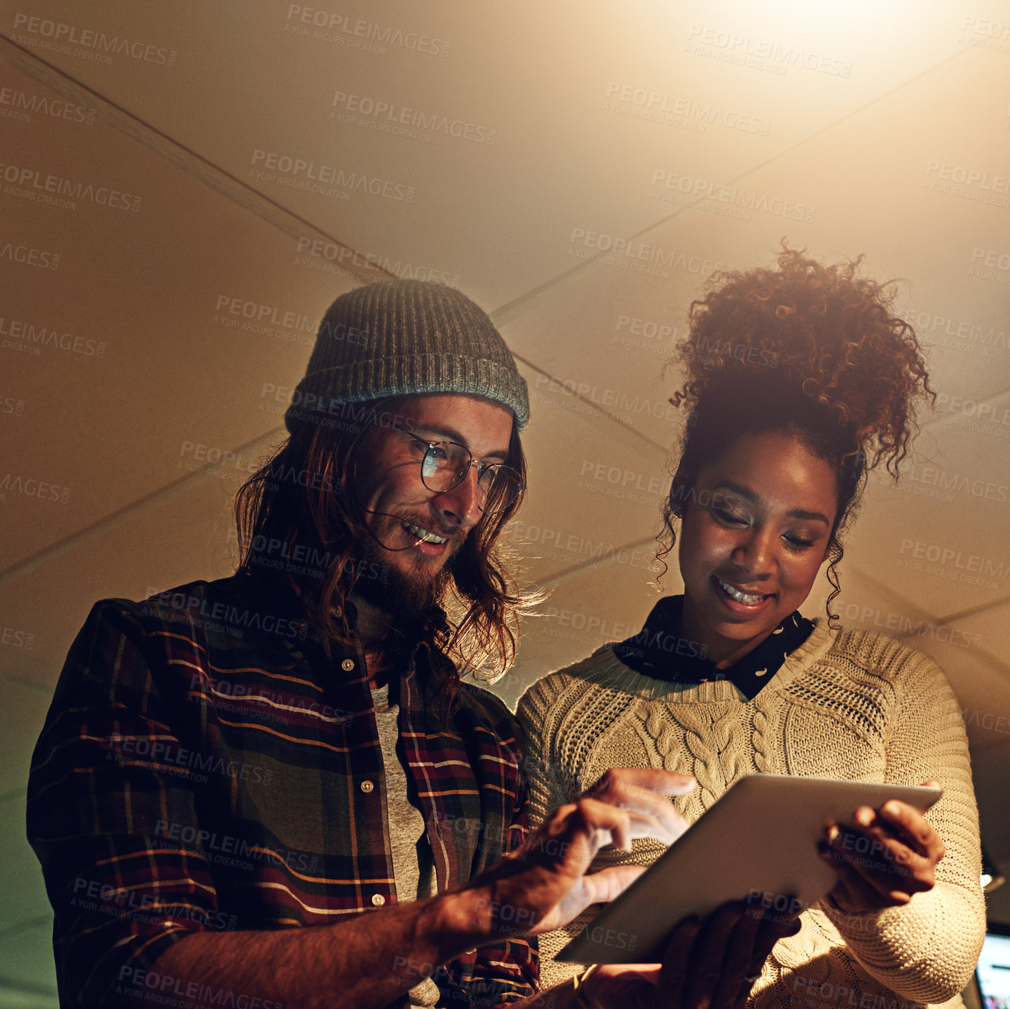 Buy stock photo Shot of two coworker discussing something on a digital tablet while working night shift at the office