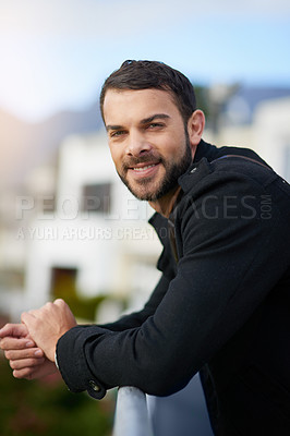 Buy stock photo Shot of a handsome young man leaning against a railing outside
