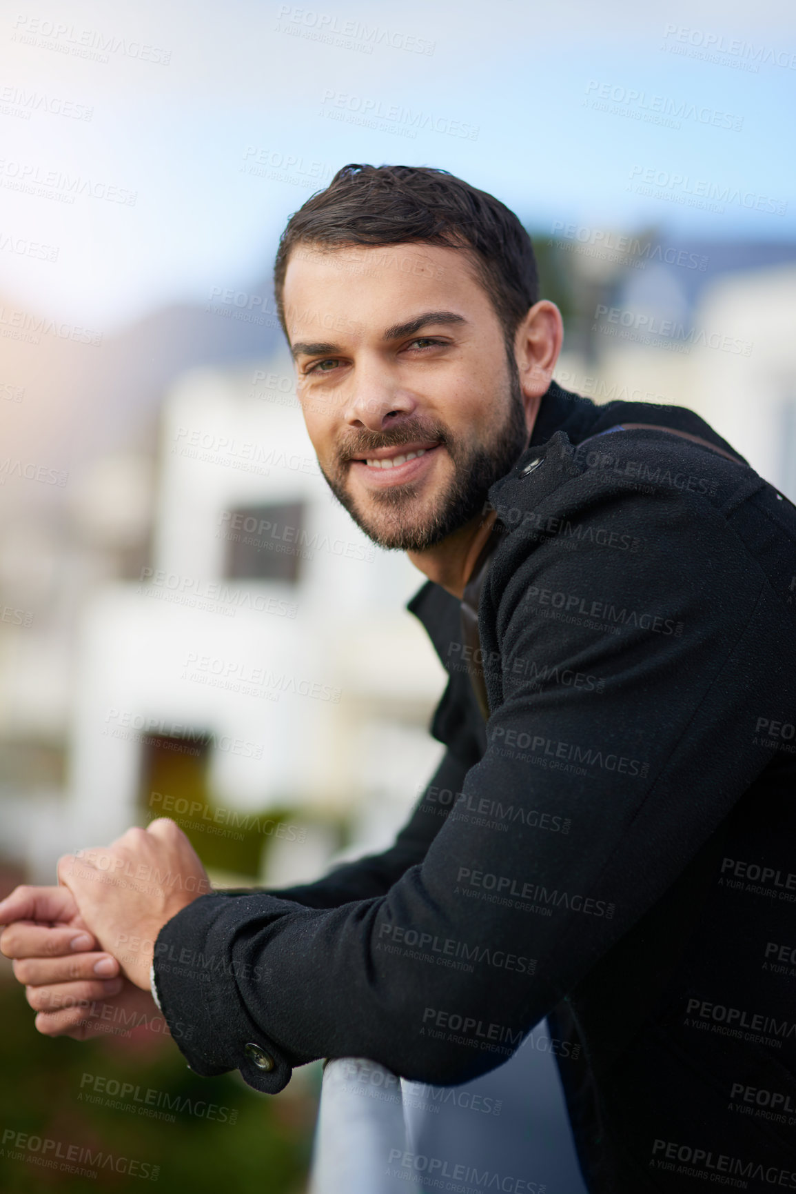 Buy stock photo Shot of a handsome young man leaning against a railing outside
