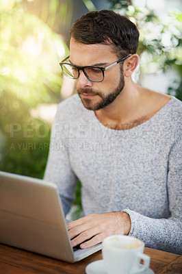 Buy stock photo Shot of a handsome young man using a laptop at an outdoor cafe