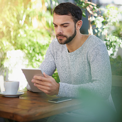 Buy stock photo Shot of a handsome young man using a digital tablet at an outdoor cafe