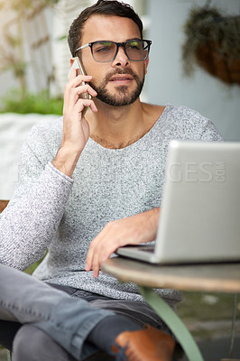 Buy stock photo Shot of a handsome young man using his phone and laptop at an outdoor cafe