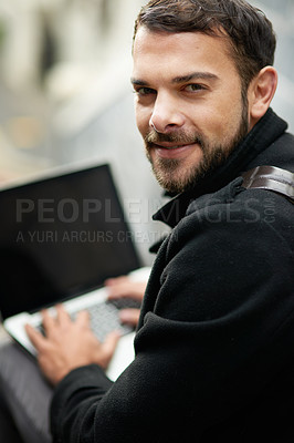 Buy stock photo Shot of a handsome young man using a laptop outside