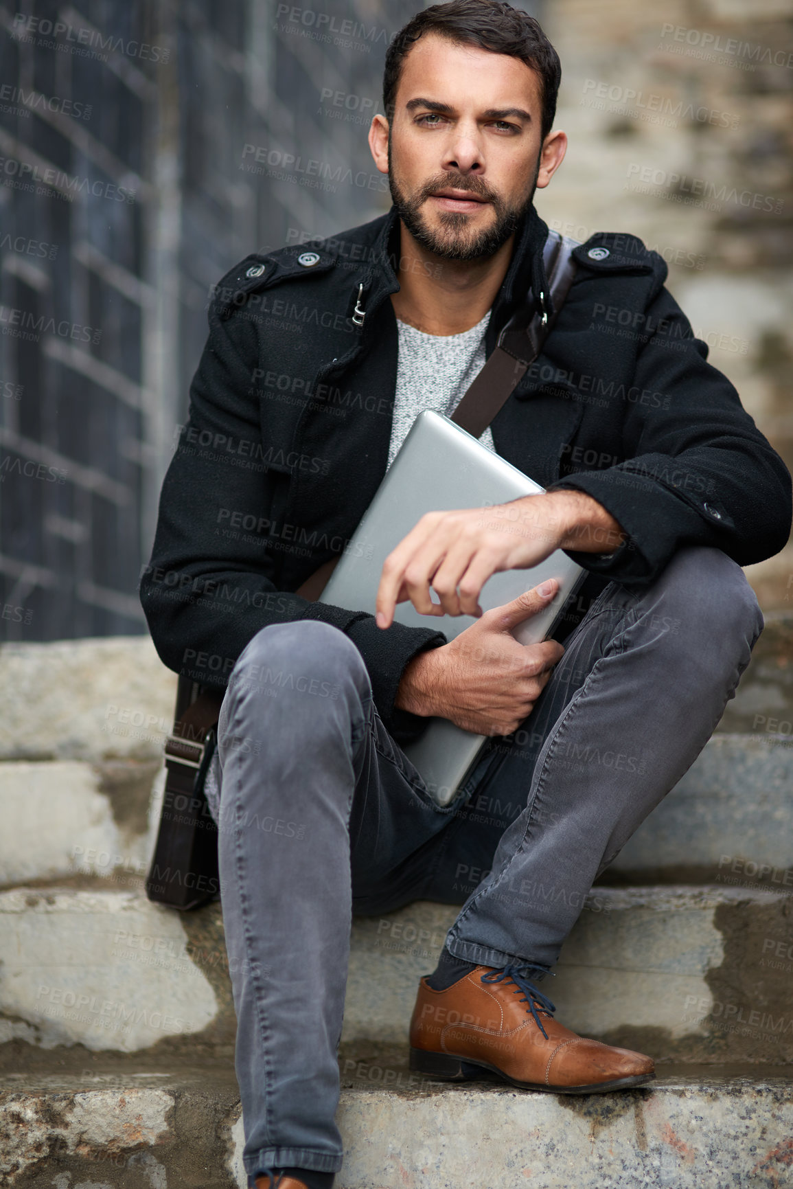 Buy stock photo Shot of a handsome young man sitting on urban steps and holding a laptop
