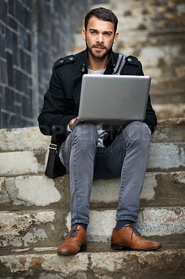 Buy stock photo Shot of a handsome young man sitting on urban steps and using a laptop