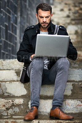 Buy stock photo Shot of a handsome young man sitting on urban steps and using a laptop