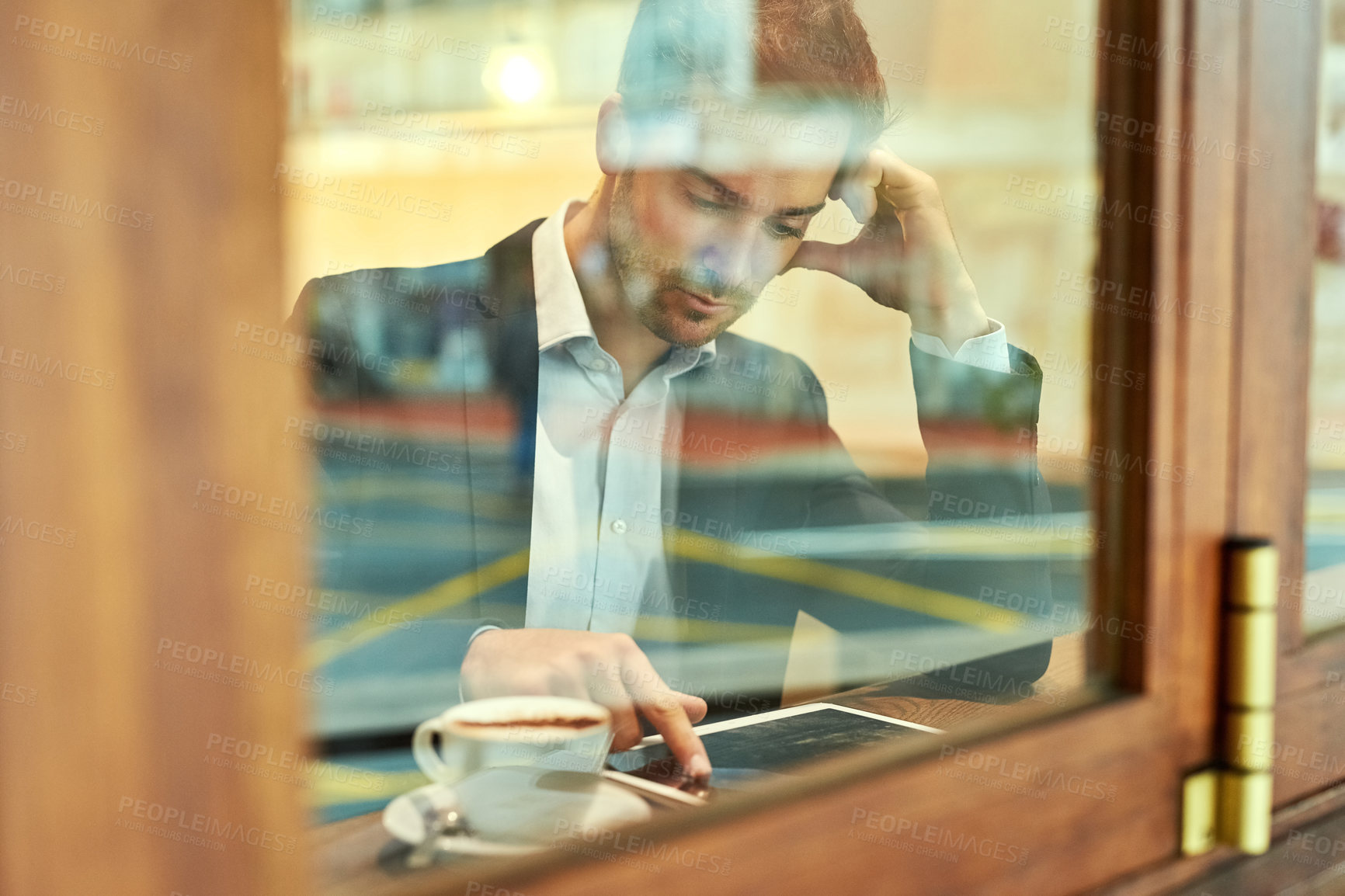Buy stock photo Shot of a young businessman using his tablet while sitting in a coffee shop