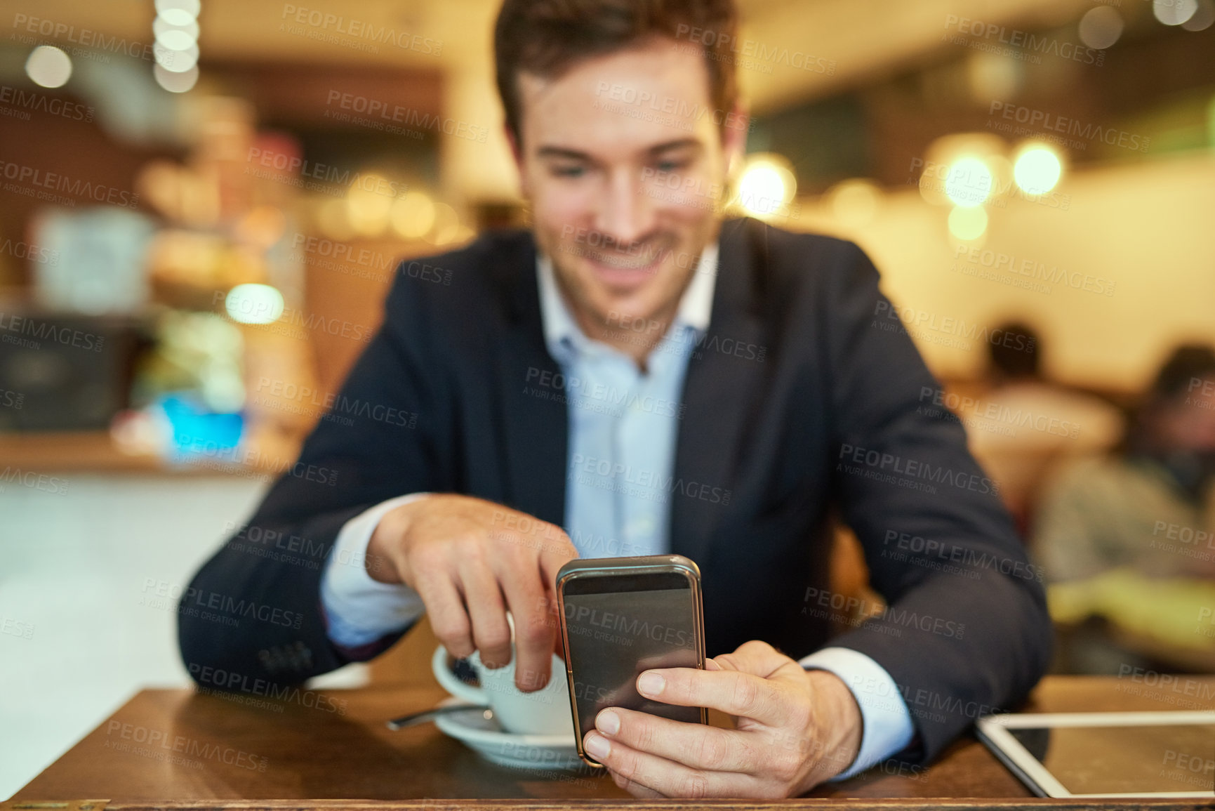 Buy stock photo Shot of a young businessman sending a text message while sitting in a coffee shop