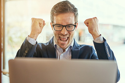 Buy stock photo Shot of a young businessman cheering while using his laptop while sitting in a coffee shop