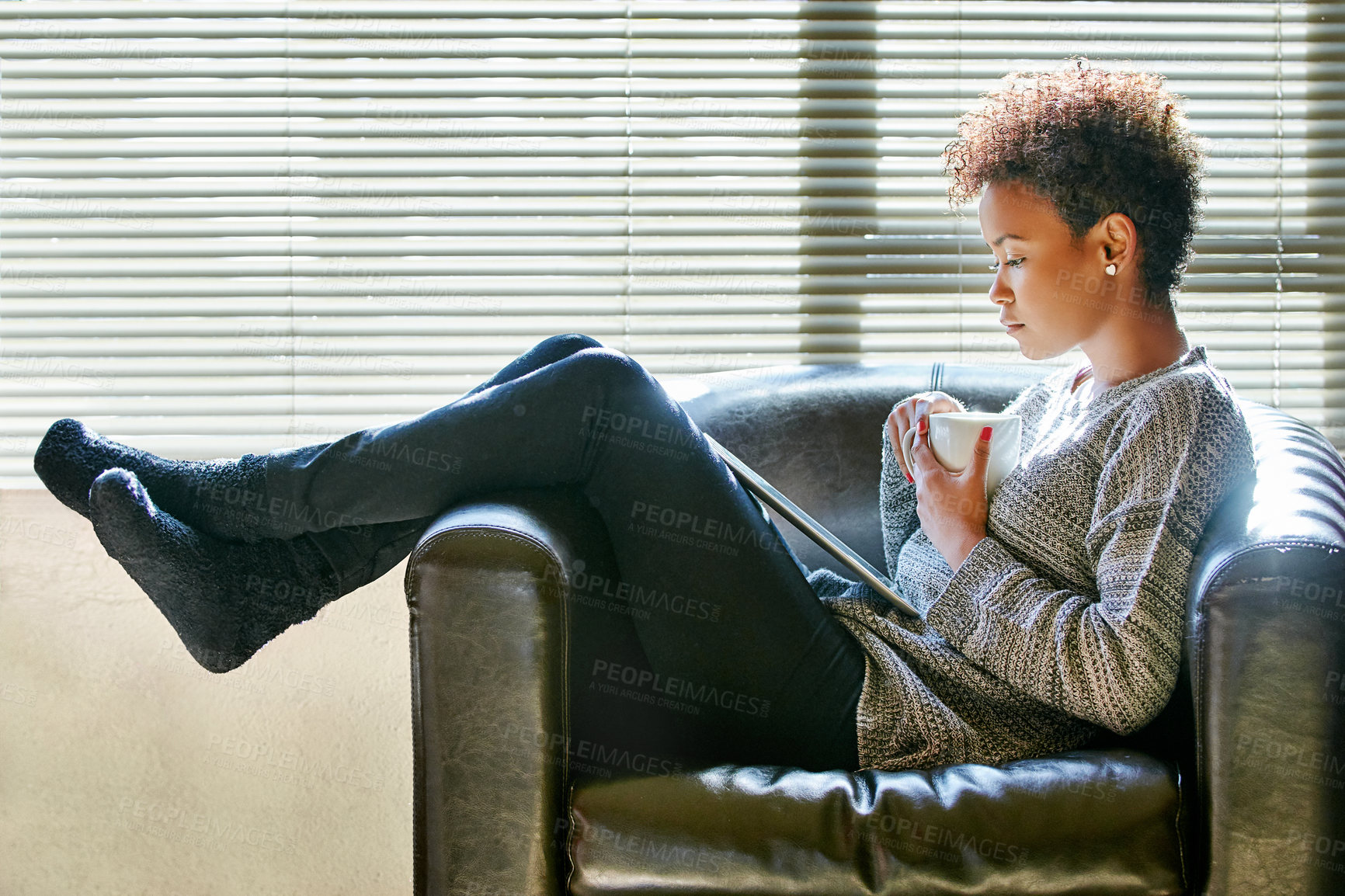 Buy stock photo Shot of a young woman enjoying a cup of coffee and using a digital tablet at home