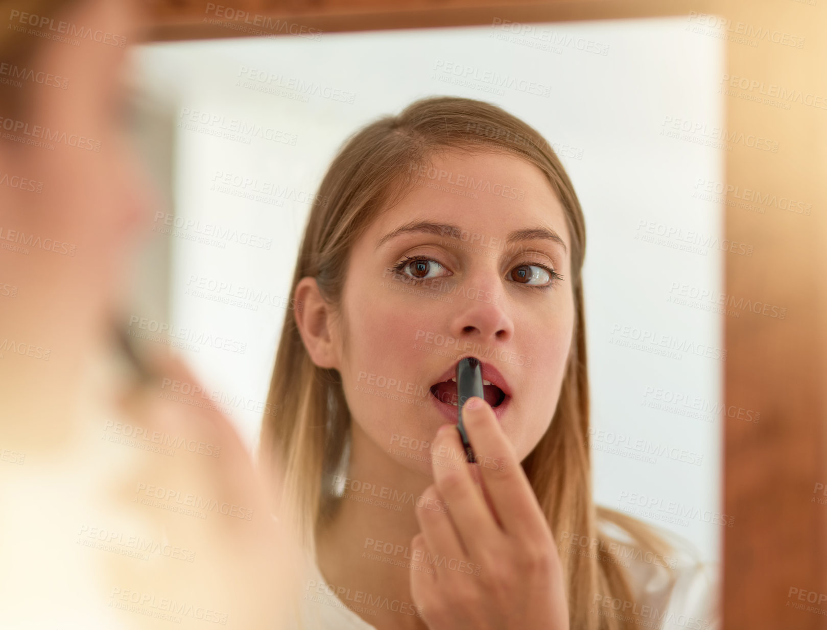 Buy stock photo Shot of a young woman applying lipstick in front of a mirror at home