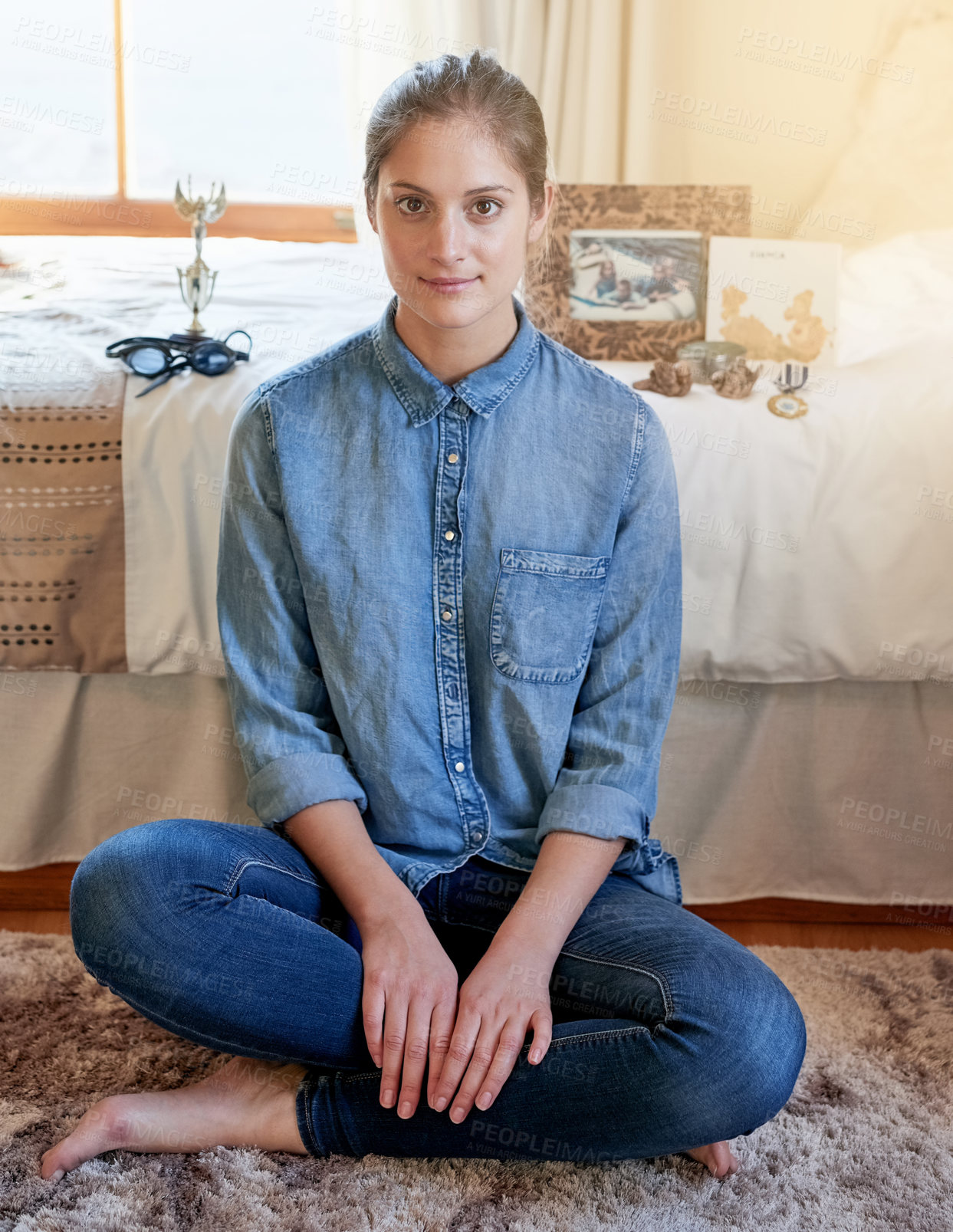 Buy stock photo Portrait of a young woman sitting on her bedroom floor with memorabilia arranged on the bed behind her