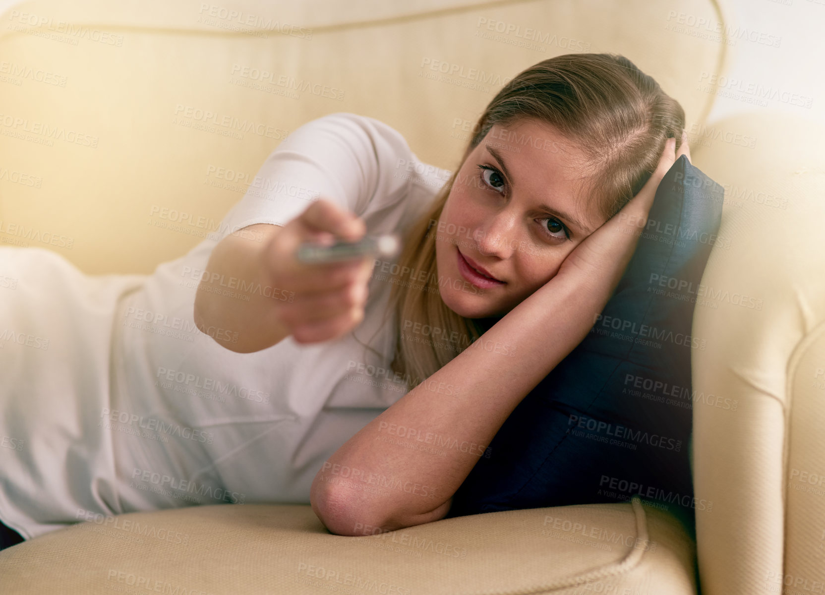 Buy stock photo Portrait of a young woman using a remote to change the channels on her TV at home