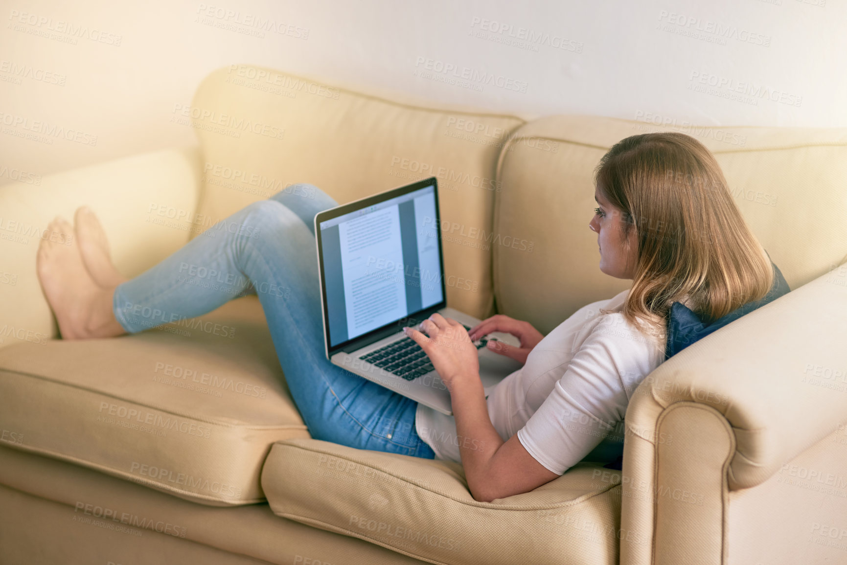 Buy stock photo Shot of a young woman using her laptop while sitting on the couch at home