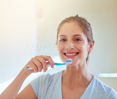 Buy stock photo Portrait of a young woman brushing her teeth in a bathroom