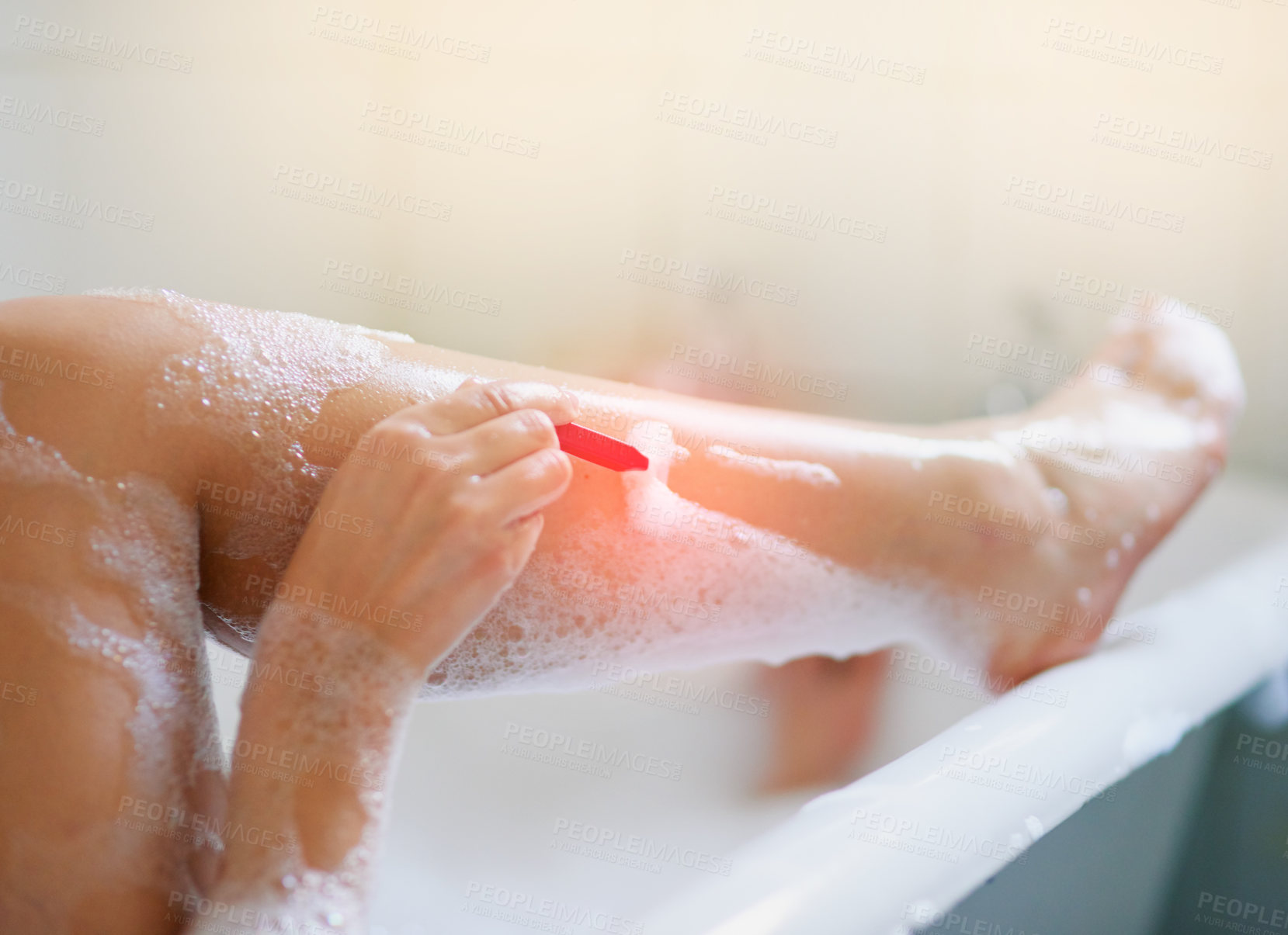 Buy stock photo Cropped shot of a woman shaving her legs while taking a bath